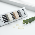 Sleek vent-clip air fresheners in soft neutral colors on a white air vent grille with eucalyptus sprigs