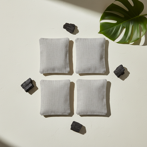 Overhead flat-lay of four linen bamboo charcoal bags with charcoal pieces and a green leaf